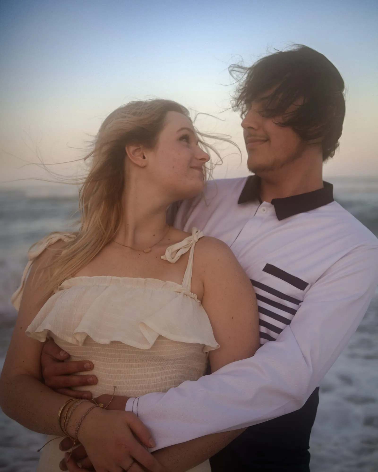 A couple embracing on a Stuart, Florida beach in warm golden sunset light, hair caught in the ocean breeze