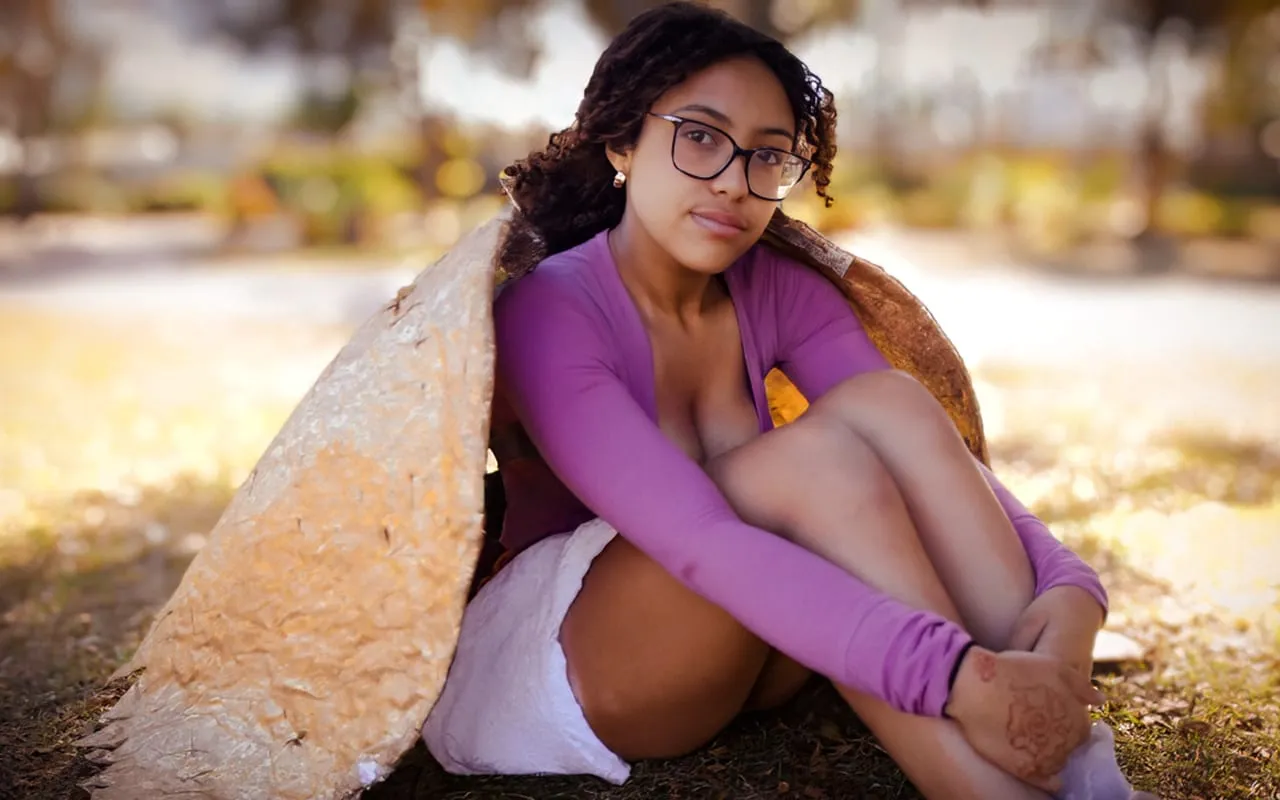 A young woman wrapped in handmade leaf wings, sitting in warm golden afternoon light in a Florida park
