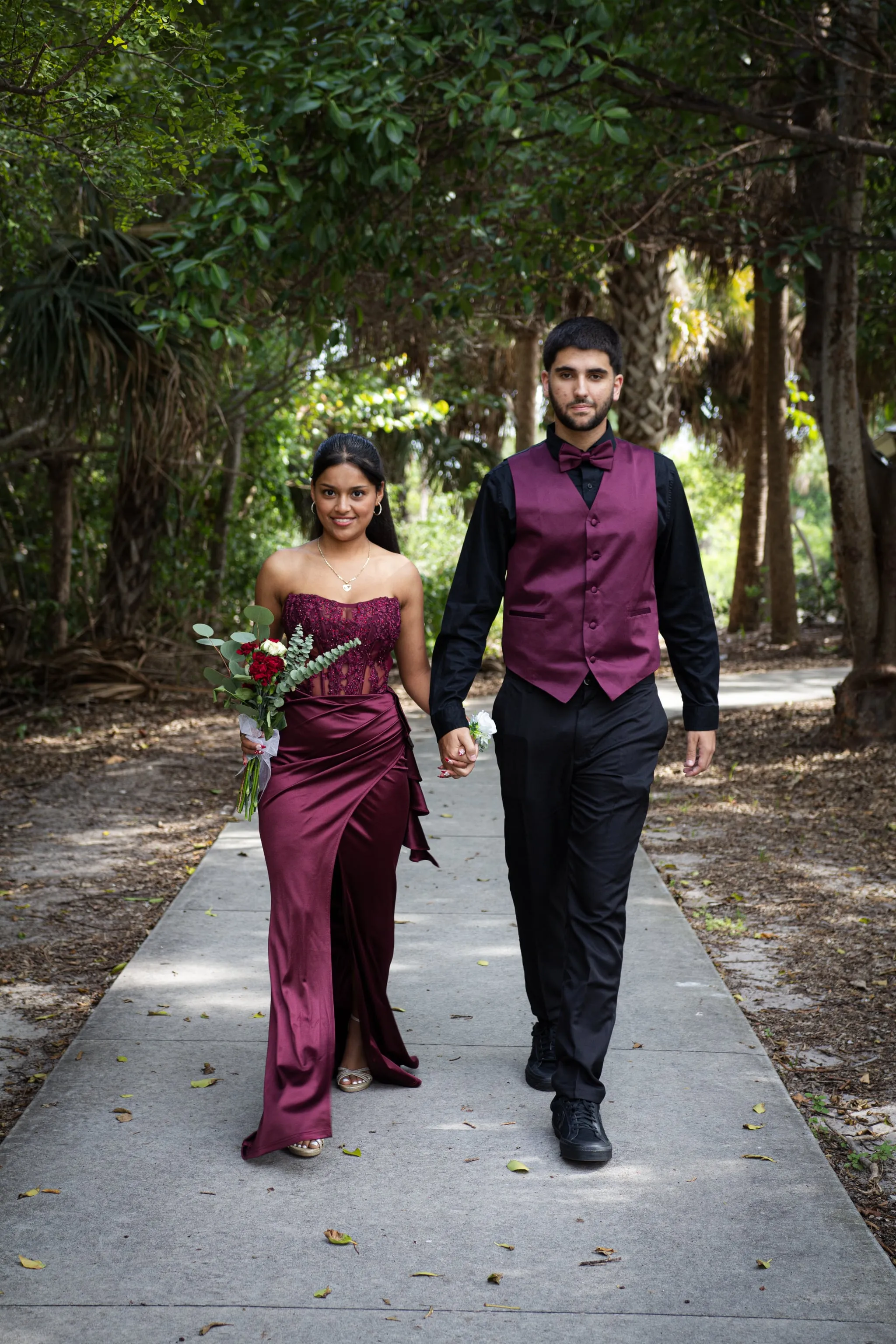 A couple in formalwear walking a tree-lined path in soft Florida afternoon light