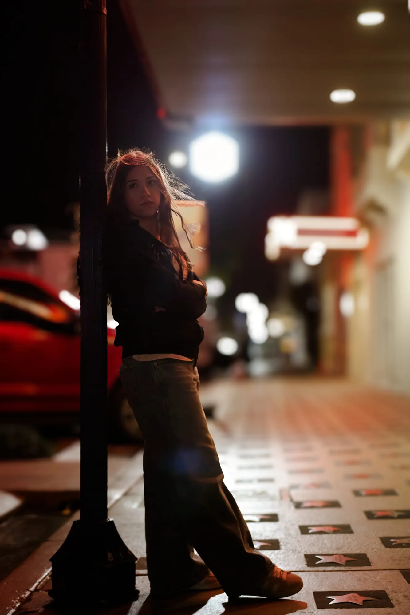 Editorial night portrait of a young woman leaning against a lamppost on a glowing downtown street